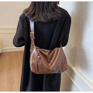 Brown leather tote bag featuring adjustable wide strap and gold metal ball charm detail