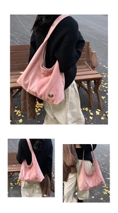 Detailed view of pink suede hobo bag featuring gold heart logo in autumn park setting