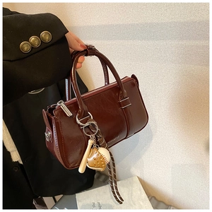 Détail d'un sac à main en cuir ciré marron foncé avec un accessoire de baseball