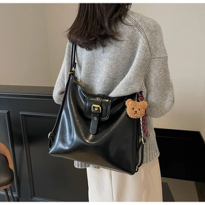 Back view of a large black glossy leather shoulder bag with buckle and bear charm