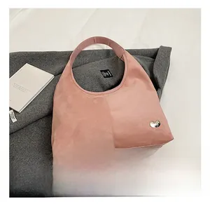 Detailed close-up of pink suede hobo bag featuring silver heart-shaped metal logo emblem