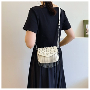 Detail of white crossbody bag with silver rivets and long fringe hanging from the bottom