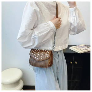Detail of brown leather crossbody bag featuring rhinestone cover and metal chain tassels