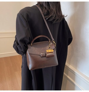 Detail view of a vintage dark brown leather crossbody bag with a mini charm on a model