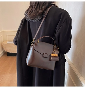 Detail of a dark brown leather crossbody bag with vintage gold buckle and charm