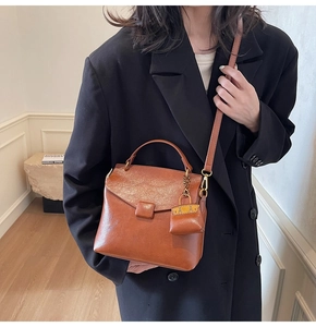 Close-up of brown vintage leather shoulder bag with decorative pendant and crossbody strap