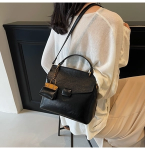 Detail of black textured leather shoulder bag featuring a mini yellow bag charm and square buckle