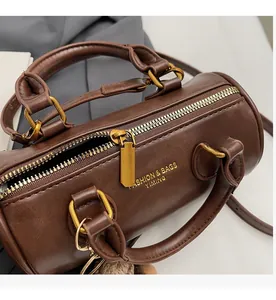 Detailed close-up of the smooth golden metal zipper closure on the brown cylinder bag