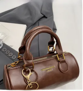 Detail of a brown leather cylinder bag with gold hardware and embossed fashion logo