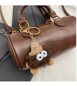 Close-up of a fuzzy brown plush charm with googly eyes and a knit hat on a leather bag