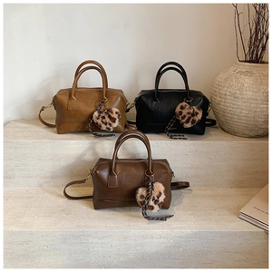 Trois sacs Boston classiques en marron et noir avec breloques cœur sur marches en pierre