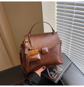 Detailed close-up of dark brown vintage faux leather handbag with metal chain charm