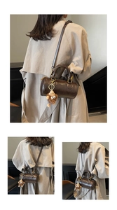 Close-up of brown leather cylinder bag with gold lettering and a cute plush monster charm