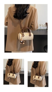 Detail of cream cylinder crossbody bag with brown trim and plush charm on camel blazer