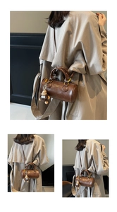 Brown cylinder Boston bag detail with plush monkey charm and shoulder strap