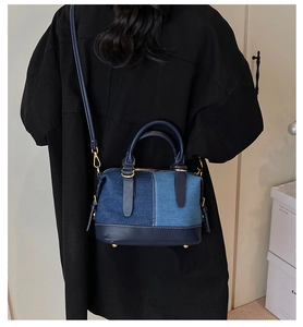 Detail of color-block denim Boston bag with contrast stitching and golden metal studs
