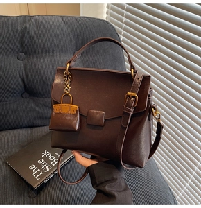 Detail of dark brown leather handbag with vintage gold buckle and mini bag charm accessory
