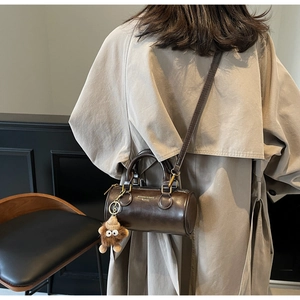 Detail of dark brown cylindrical shoulder bag featuring a cute lion plush pendant