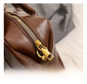 Gros plan détaillé du zip doré et du cuir PU grainé marron sur le sac bandoulière