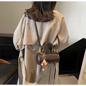 Detail of dark brown cylindrical crossbody bag with plush monkey charm and gold hardware