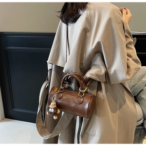 Detail of dark brown cylindrical handbag with plush monster charm and leather texture
