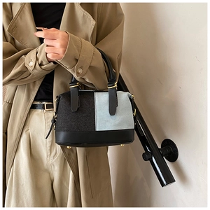 Detail of color-block denim handbag featuring black leather trim and gold metal studs