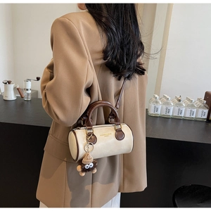 Detail of a retro cylinder bag with monster charm worn by a model in a camel blazer