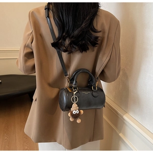 Detail of black cylindrical crossbody bag with gold zippers and plush monster charm