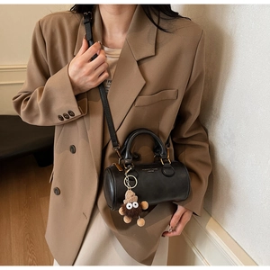 Detail of black leather cylindrical Boston bag with cute plush charm on brown suit