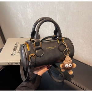 Macro view of black cylindrical handbag showing gold lettering and cute plush charm detail