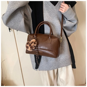Détail du sac Boston marron foncé avec charm cœur léopard porté par un mannequin