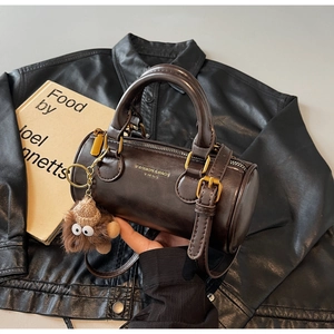 Close-up of brown cylinder bag with gold hardware and a cute monster plush charm