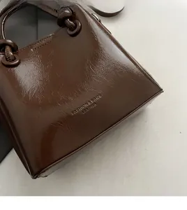 Détail du sac seau en cuir marron foncé avec lettrage embossé et bandoulière à nœuds