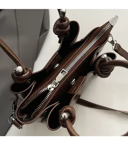 Détail macro du sac à main en cuir marron avec fermeture éclair argentée et anse nouée