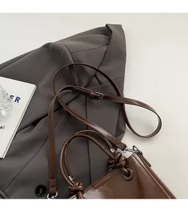 Détail du sac seau en cuir marron foncé avec poignée tressée sur une veste grise