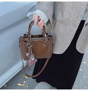 Détail d'un sac cabas en cuir marron foncé avec poignées rondes et ours peluche