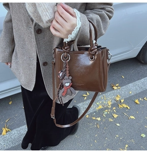Détail du sac cabas en cuir marron foncé avec poignée nouée et breloque ours