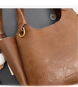 Détail du sac seau en cuir marron avec grain texturé, ferrures dorées et breloque baseball
