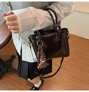 Détail d'un sac seau en cuir verni marron foncé avec un joli pendentif de lapin