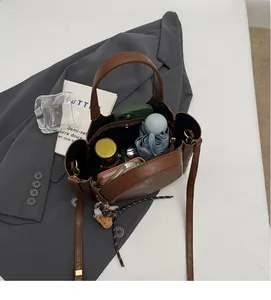 Vue de dessus d'un sac seau marron spacieux rempli d'essentiels sur un blazer gris