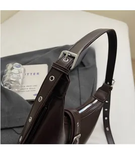 Dettaglio tracolla regolabile in pelle marrone con occhielli argentati su borsa
