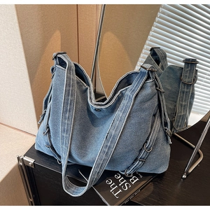 Macro shot of light blue denim tote bag with layered straps and metal rings on a black surface