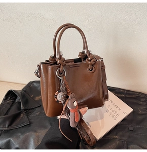 Détail du sac seau en cuir ciré marron avec anses en métal et breloque ours