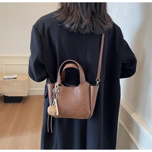 Détail du sac seau en cuir marron vintage avec logo embossé et pendentif élégant