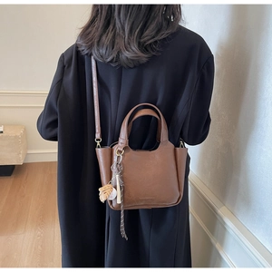 Sac seau vintage en cuir marron avec breloque baseball porté sur un manteau noir