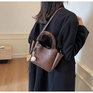 Détail du sac seau rétro en cuir marron avec texture grainée et breloque décorative