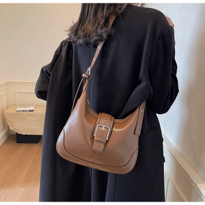 Dettaglio borsa a spalla in pelle marrone con fibbia argentata su modella in posa