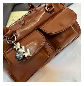 Detail of glossy brown leather tote bag featuring twin front pockets and a heart-shaped charm