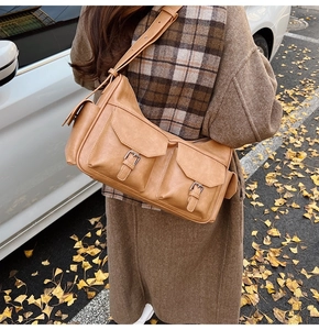 Detail of khaki vintage shoulder bag with utility pockets and metal buckles outdoors