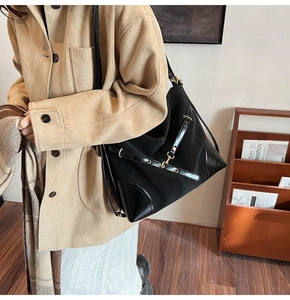 Detail of a black nylon tote with glossy leather trim and metallic gold accents on a model